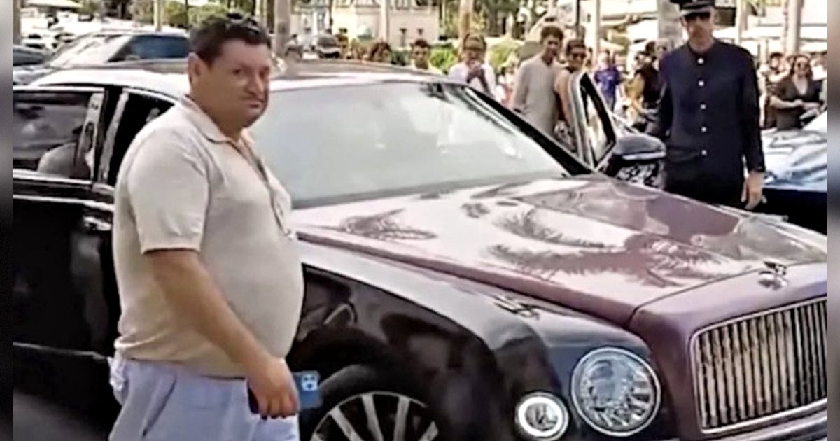 Man standing next to a luxury car, surrounded by a crowd of onlookers in an urban setting.
