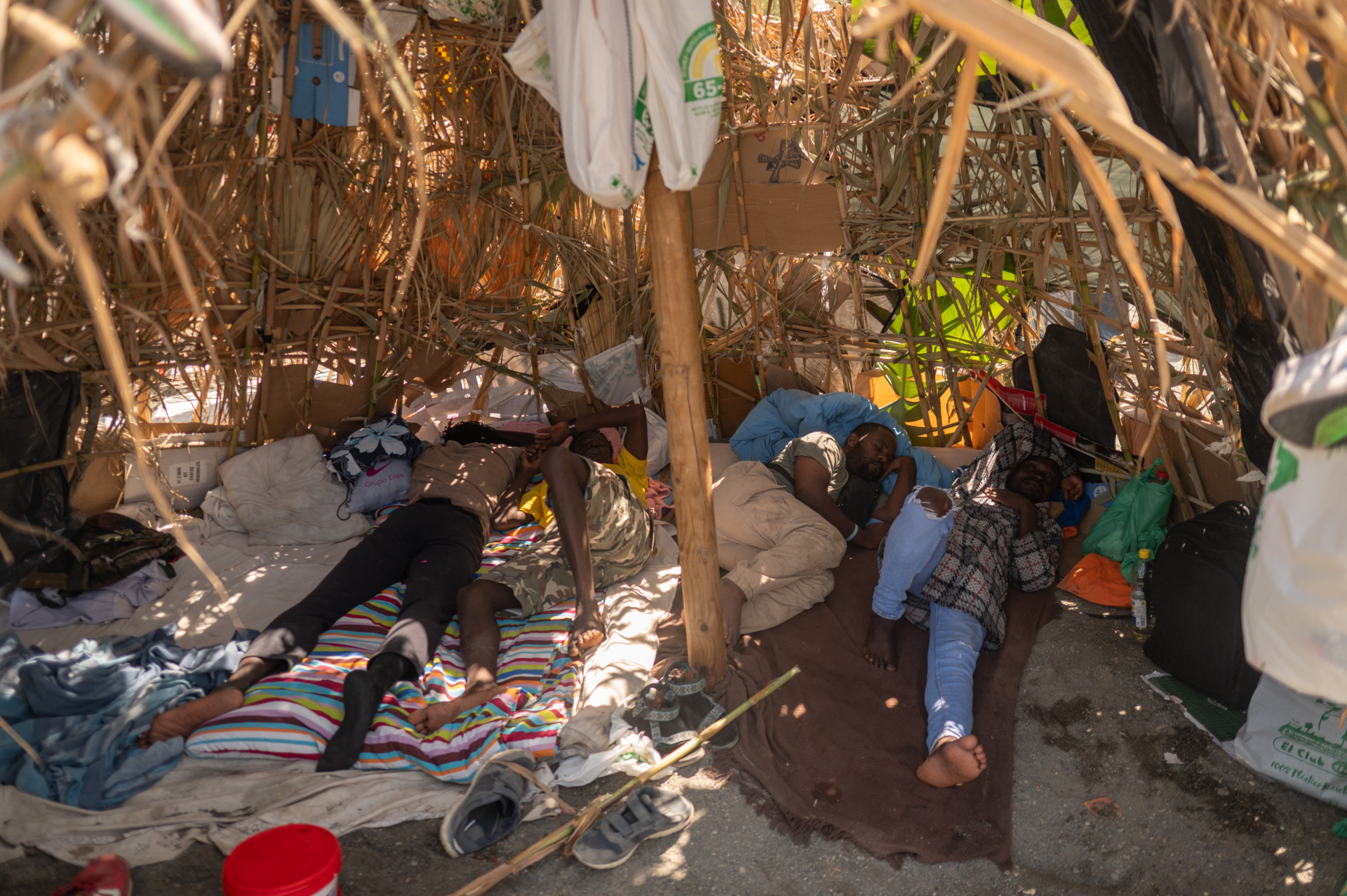 Migrants rest under a makeshift shelter as they wait to enter a short-stay migrants centre CETI at Trampolin beach in Spain's north Africa's Ceuta enclave on August 15, 2026. 72,000 would-be migrants crossed from Morocco to the Spanish exclave of Ceuta last month. According to a recent survey by the ONDH, 74 percent of 500 young people living near the border said they followed accounts or content related to preparing to emigrate. (Photo by JORGE GUERRERO / AFP via Getty Images)